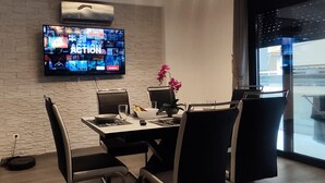 Une chambre moderne avec un mur en briques, un téléviseur à écran plat diffusant différentes chaînes, une table à manger avec des chaises et une orchidée en pot.