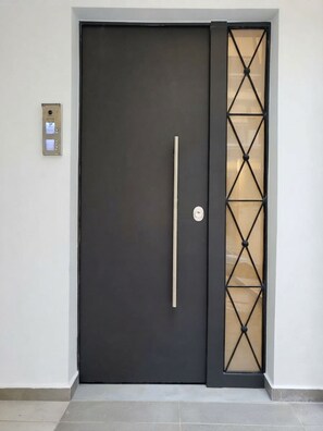 Een moderne deur met een verticale handgreep en een ruitpaneel met een geometrisch patroon.