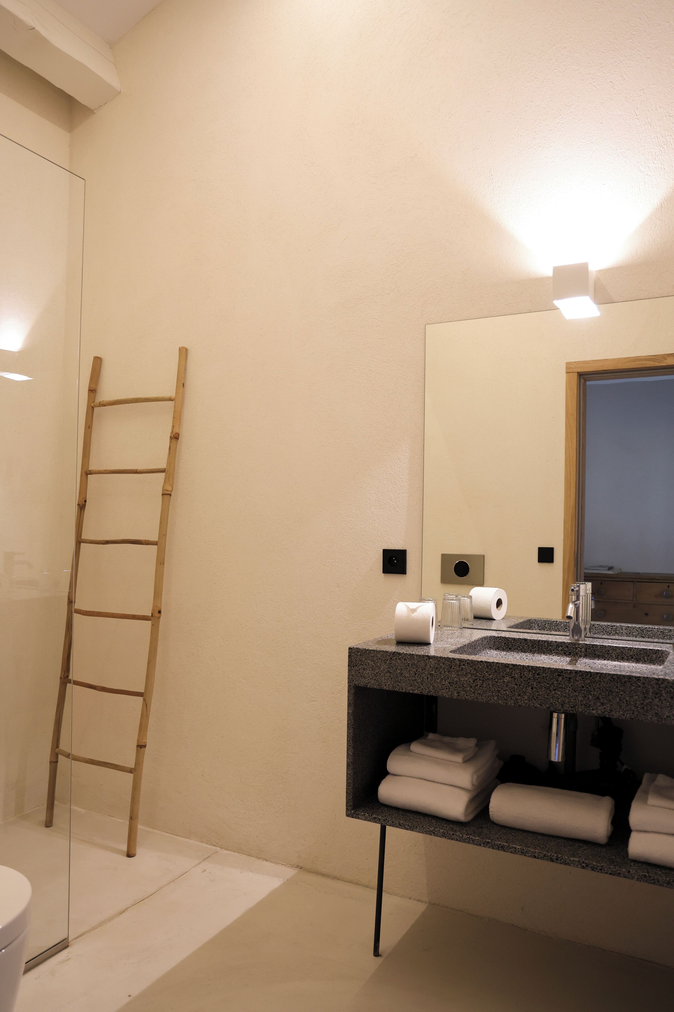 Un baño con una escalera de madera, un lavamanos con toallas y un espejo con luces.