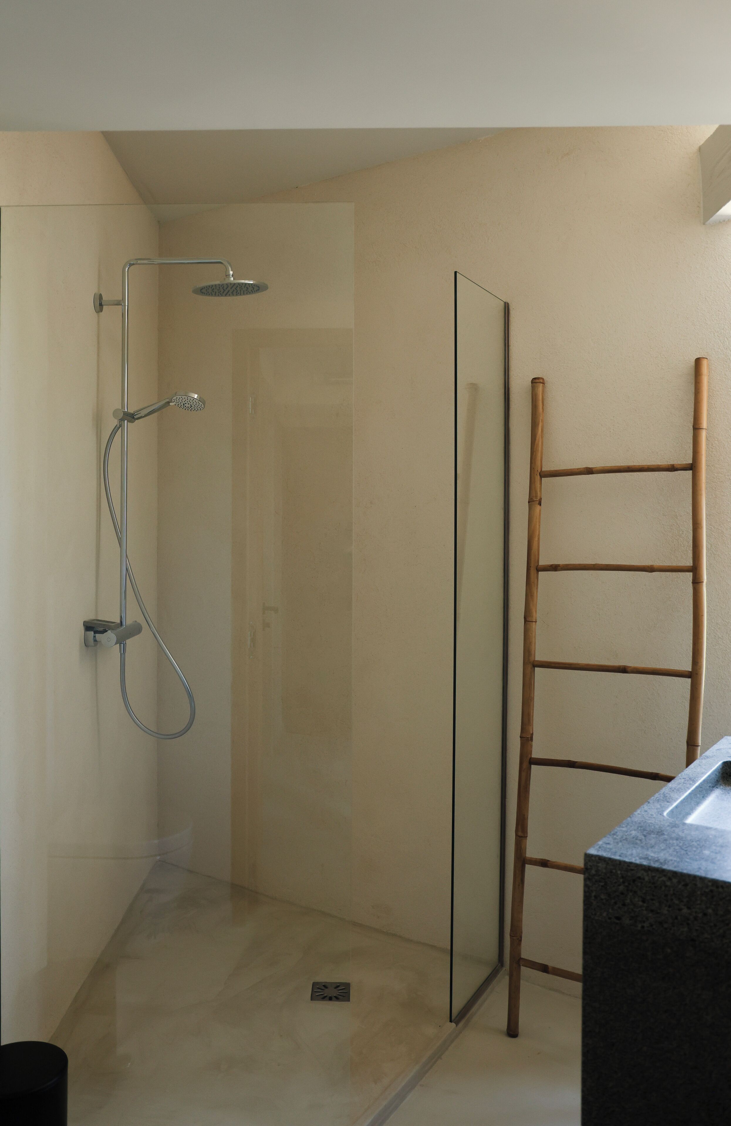 Une douche avec une porte en verre, une échelle en bambou et un lavabo en marbre.