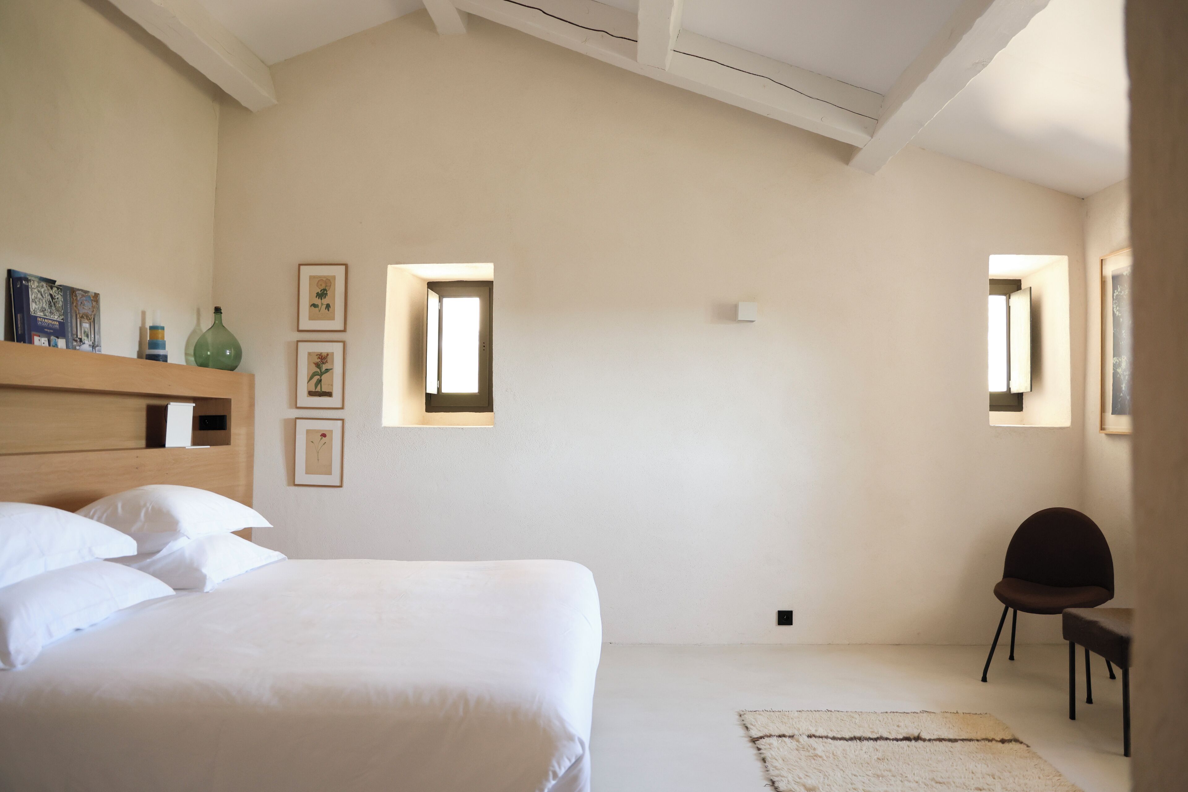 A bedroom with a large bed, a chair, a small table, and framed pictures on the wall.
