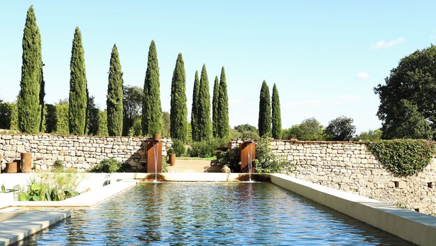 A serene pool area with a stone wall and tall cypress trees in the background. - PRIEURÉ SAINT NICOLAS - LES MAISONS (Sainte-Anastasie)