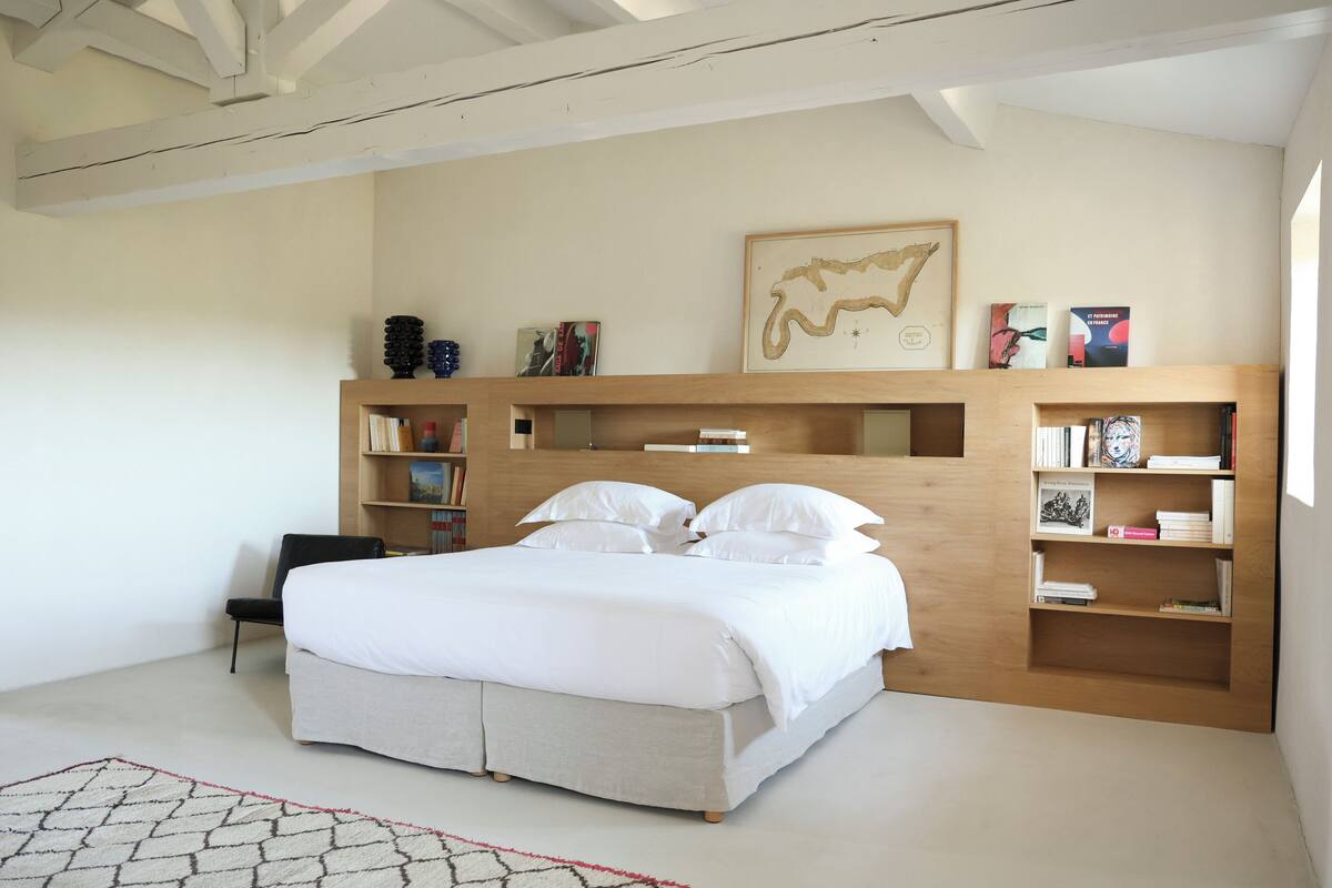 A bedroom with a large bed, built-in bookshelves, a chair, and a map artwork on the wall.