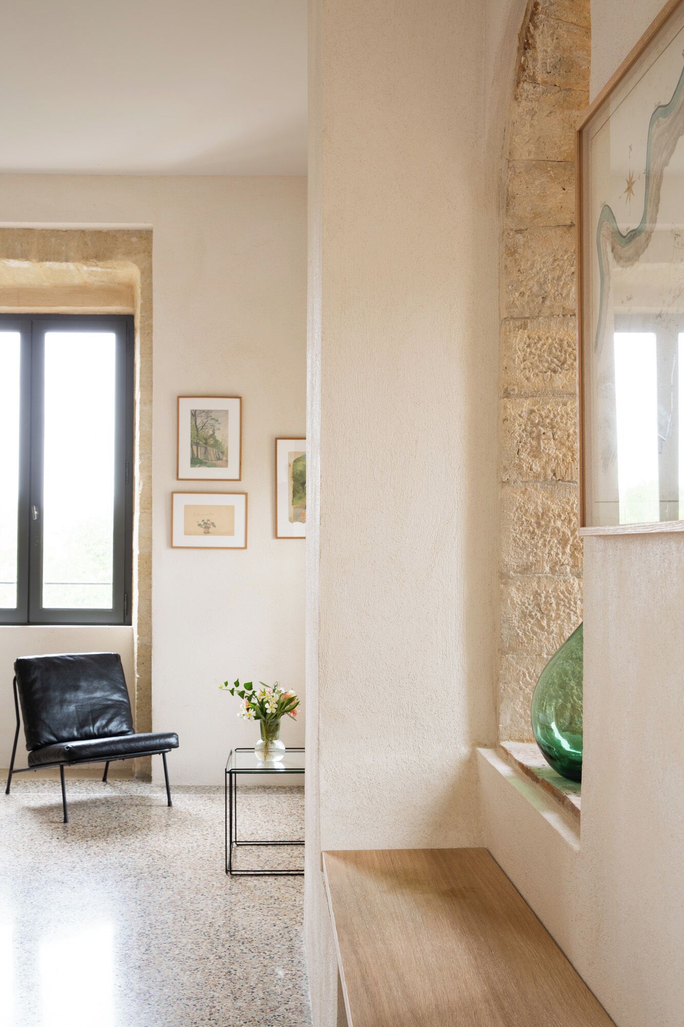 A room with a black leather chair, a glass table with a vase of flowers, and framed artwork on the wall.