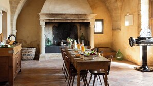 A rustic dining area with a stone fireplace, wooden furniture, and a tiled floor. - PRIEURÉ SAINT NICOLAS - LES MAISONS (Sainte-Anastasie)