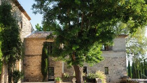 A stone building with a tiled roof, a gravel pathway, and a large tree in front. - PRIEURÉ SAINT NICOLAS - LES MAISONS (Sainte-Anastasie)