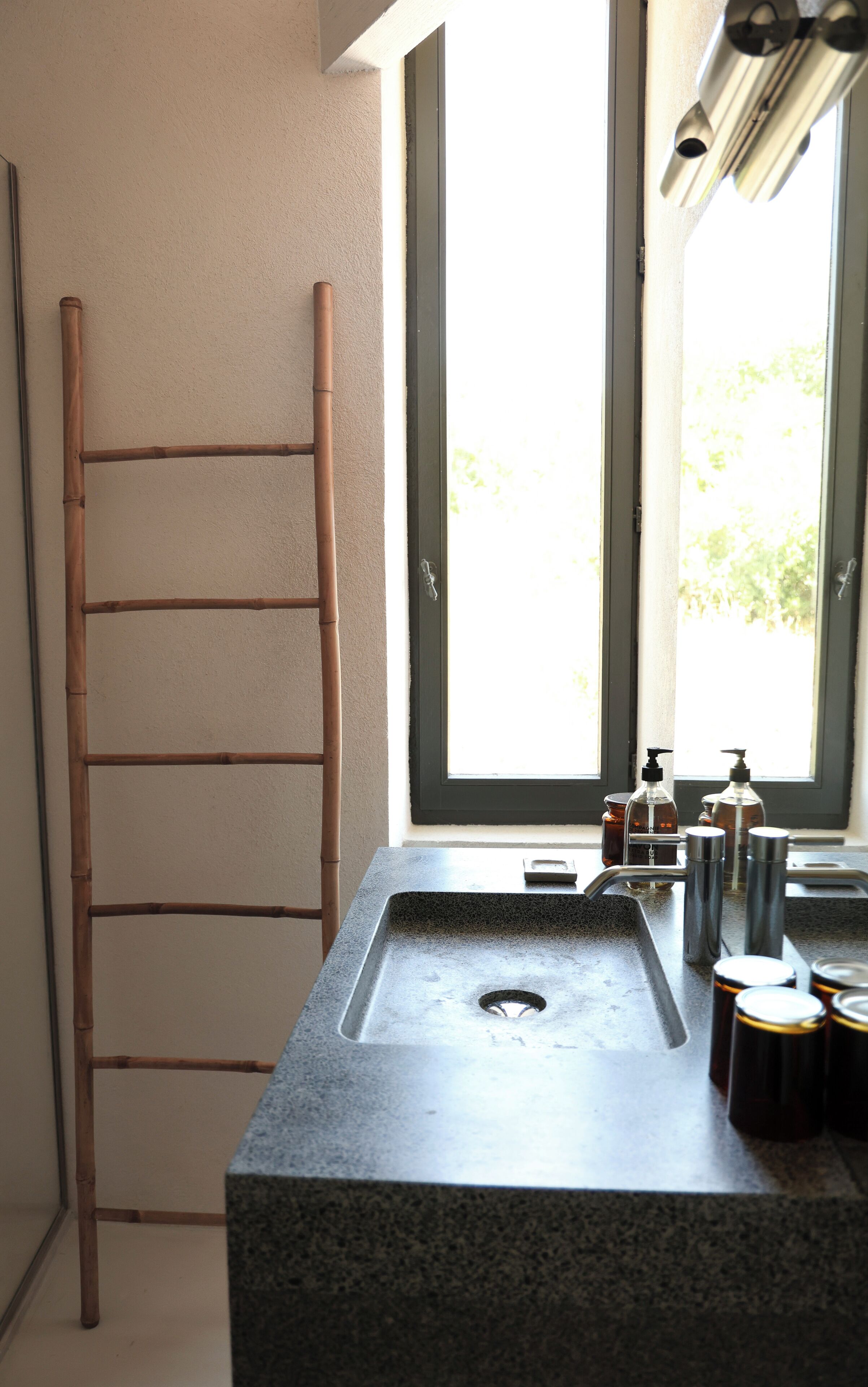 Un baño con lavamanos de granito, escalera de madera y ventana con vista a la vegetación exterior.