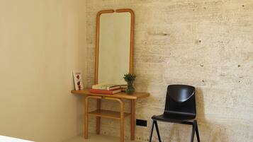 A room with a bed, a wooden desk, a black chair, a mirror, and a small plant.
