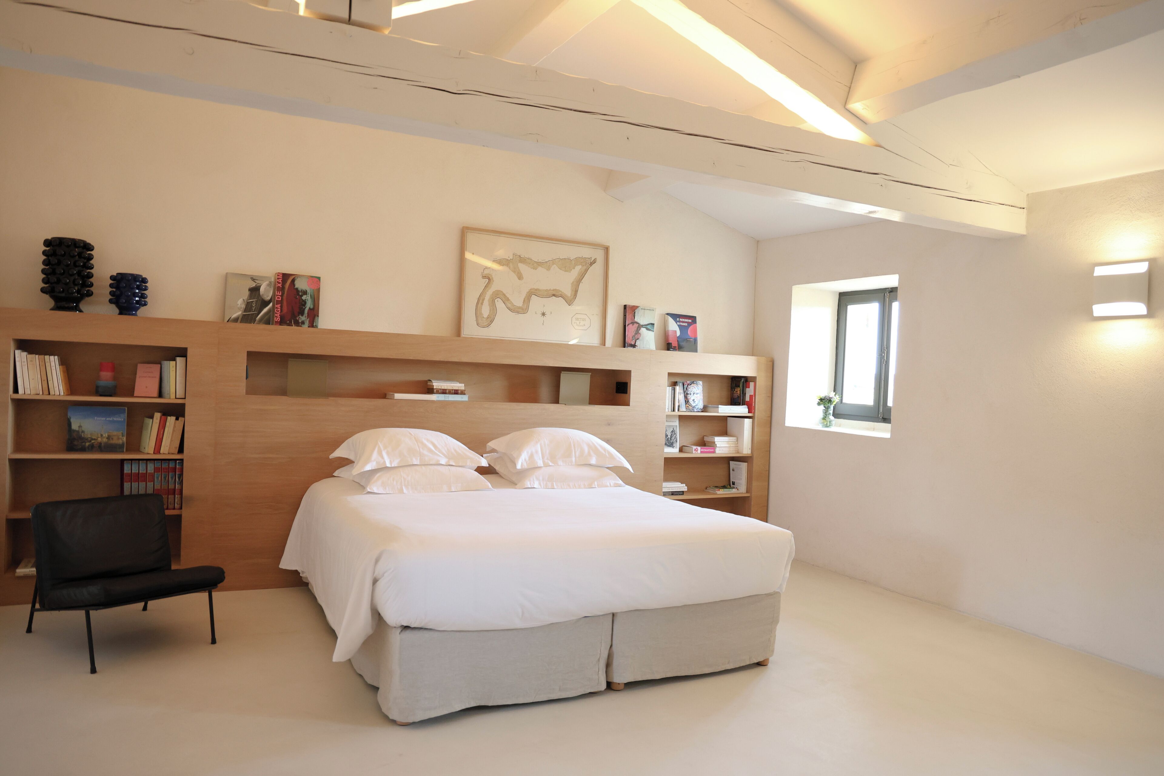 A modern bedroom with a large bed, built-in bookshelves, a desk, and a window with natural light.