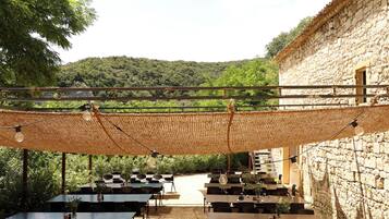 An outdoor dining area with tables and chairs, a stone building, and a view of a hillside.