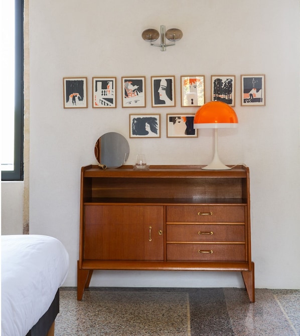 A bedroom with a wooden dresser, a bed, and a wall with framed artwork. - PRIEURÉ SAINT NICOLAS - LES MAISONS (Sainte-Anastasie)