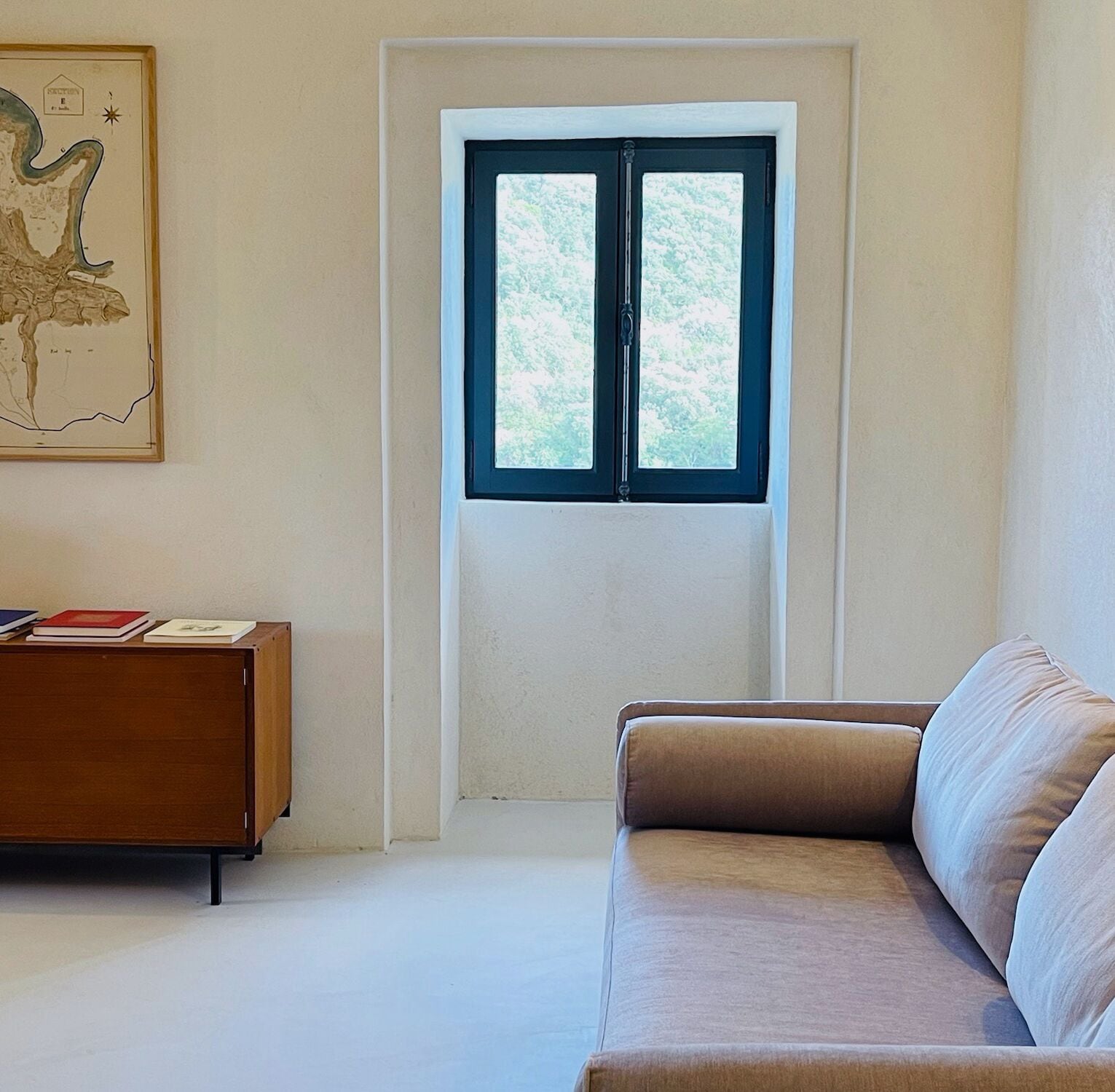 A room with a large window, a sofa, a wooden cabinet, and a framed artwork on the wall.