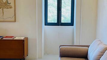 A room with a large window, a sofa, a wooden cabinet, and a framed artwork on the wall.