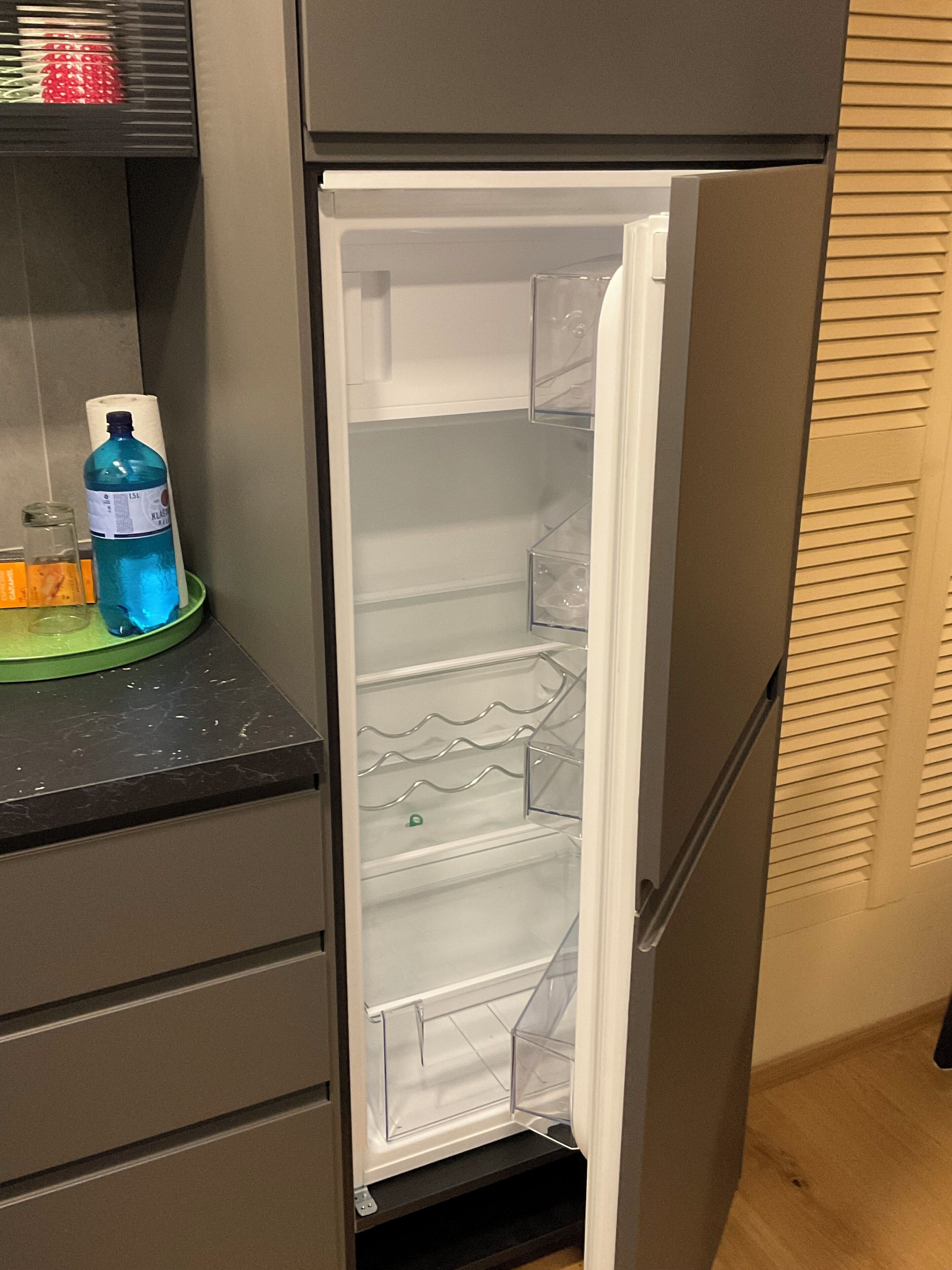 A refrigerator with a clear interior, a bottle of water, and a roll of paper towels on the door shelf.