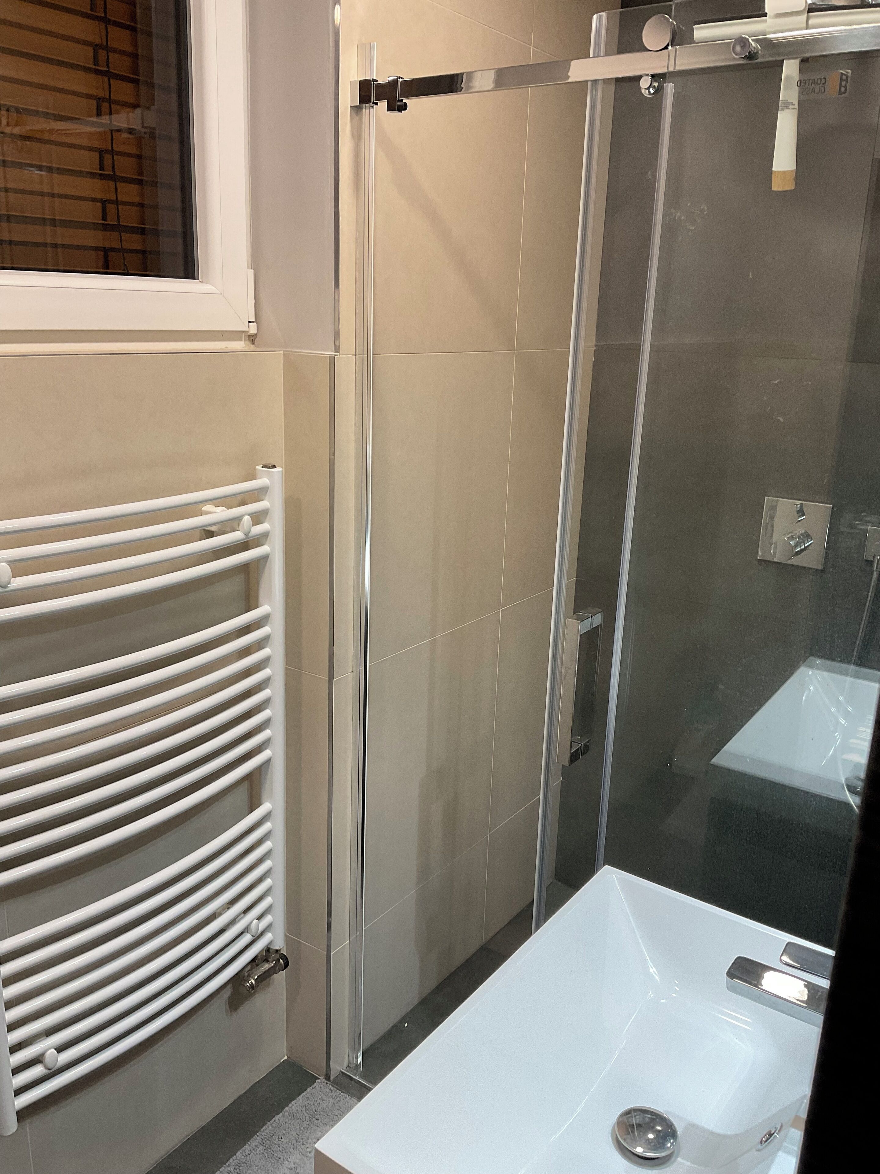 Un baño moderno con cabina de ducha de vidrio, una bañera blanca y un toallero blanco.