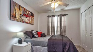 A bedroom with a bed, nightstand, lamp, ceiling fan, and a painting on the wall. - Rare Disney-Area Waterfront Retreat | Pool & Fountain Views (Kissimmee)