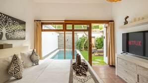A modern bedroom with a large bed, a TV, and a view of a swimming pool and garden. - Cozy 2 Bedroom Villa in Seminyak with private Pool (Seminyak - Bali)