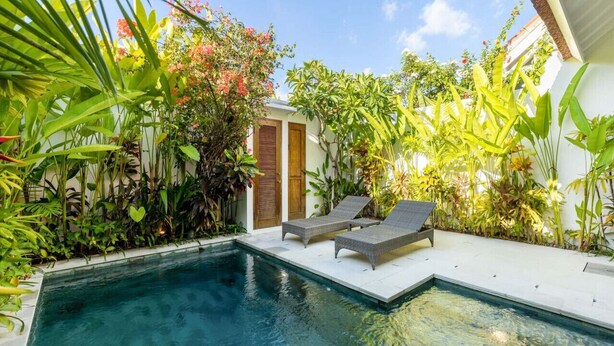 Una piscina con sillas de descanso y exuberante vegetación tropical.
