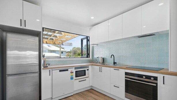 Una cocina moderna con armarios blancos, un refrigerador de acero inoxidable, horno empotrado y una ventana con vistas al exterior.