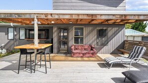 Un patio moderno al aire libre con una mesa de madera, dos sillas negras, un sofá rojo con estampado y una silla lounge a rayas.