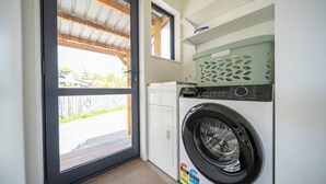 Un lavadero pequeño y funcional con lavadora y secadora de carga frontal, una ventana y una puerta al exterior.