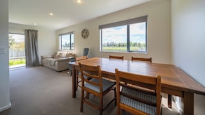 Amplia habitación con una mesa de comedor de madera, cuatro sillas, un sofá y ventanas grandes que ofrecen vistas al exterior.