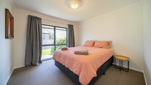 Un dormitorio con una cama, un taburete pequeño y una ventana con cortinas.