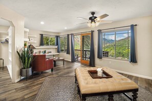 Un salon spacieux doté d’une grande fenêtre, d’un ventilateur de plafond et offrant une vue sur un paysage montagneux.