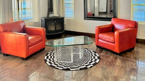 Una sala de estar con dos sillones de cuero rojo, una mesa de centro de vidrio, una chimenea negra y un espejo grande en la pared.