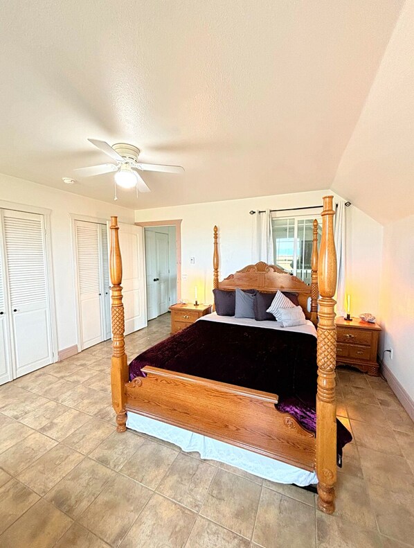 A spacious bedroom with a four-poster bed, a ceiling fan, and a large window with curtains.