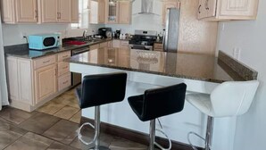 Una cocina moderna con una isla central, taburetes de bar y armarios de madera clara.