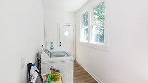 A laundry area with a washing machine, ironing board, and cleaning supplies. - Charm of Crestview! 5-bedroom house in serene Knoxville! (Knoxville)