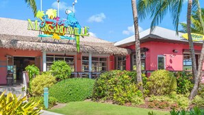 A building with a thatched roof, a colorful sign with a parrot, and a sign for 'Margaritaville.' - 1 bedroom Presidental - Margaritaville Resort, St Thomas (Saint Thomas)