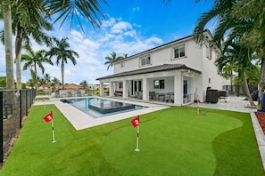 A modern house with a swimming pool, two numbered flags, and palm trees.