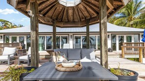 Een overdekt terras met een tafel, stoelen en plantenbakken.