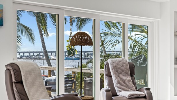Een kamer met twee fauteuils, een groot raam met uitzicht op een jachthaven en een brug, en een rieten vloerlamp.