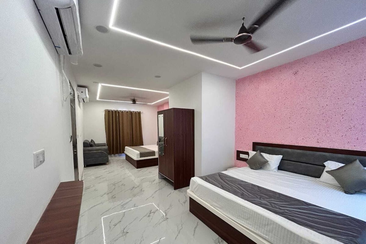 Quarto de hotel moderno com uma cama grande, guarda-roupa, área de estar com sofá e ventoinha no teto.