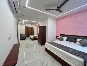 A modern hotel room with a large bed, a wardrobe, a seating area with a sofa, and a ceiling fan. - Pratibha Hotel and Restaurant (Karauli)