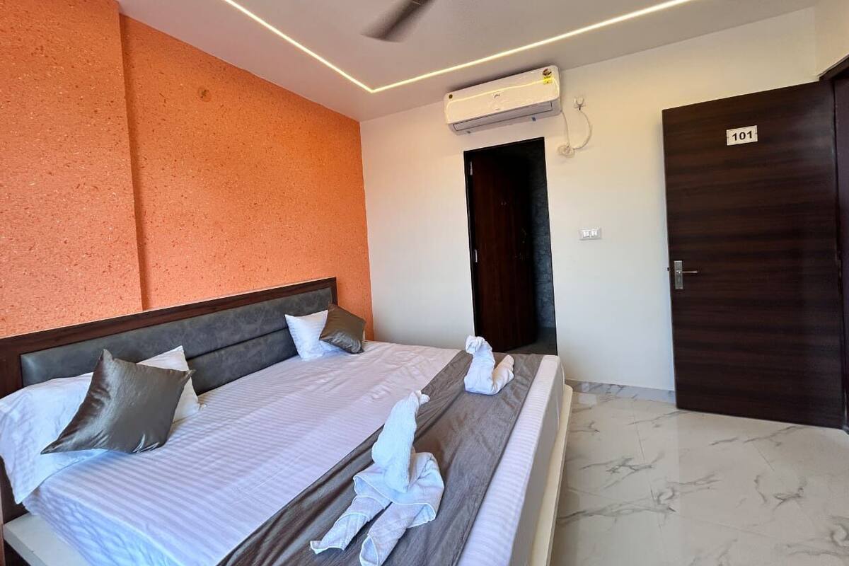 Quarto de hotel com cama, almofadas, ventoinha no teto, aparelho de ar condicionado e porta com um número.