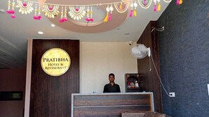 Un espace d’accueil avec une enseigne indiquant « Pratibha Hotel & Restaurant », un comptoir de réception, un ventilateur et un coin salon.