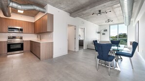 A modern kitchen with built-in appliances, a dining area with a glass table, and a view through large windows. - Milan Aventura Hotel (Ojus)