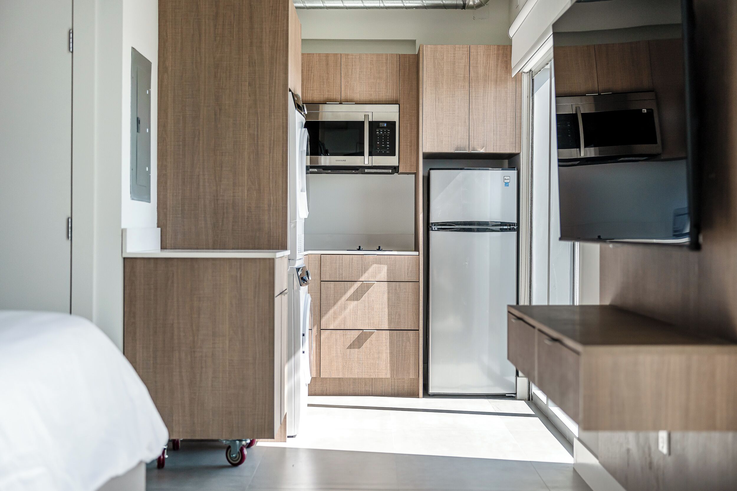 A compact kitchen with wooden cabinets, a microwave, and a refrigerator.