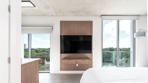 A modern bedroom with a large bed, a built-in TV, and a balcony with a city view. - Milan Aventura Hotel (Ojus)