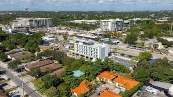 An aerial view of a residential area with multiple buildings, including a large white building with a yellow accent, surrounded by greenery and a swimming pool.