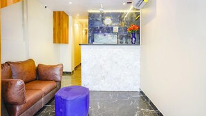 A reception area with a brown leather sofa, a purple ottoman, a marble reception desk, and a clock on the wall. - Hotel Emirates Suite (Mumbai)