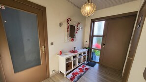 Un pasillo con piso de madera, una consola blanca con espejo, un teléfono rojo y una puerta con panel de vidrio esmerilado.