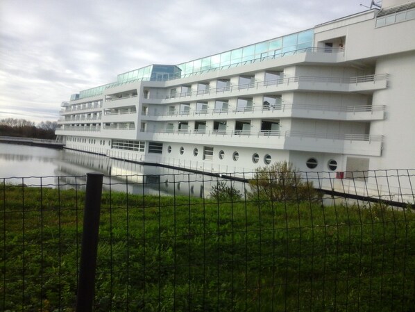 A multi-story building with balconies and a river in the foreground.
