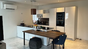 A modern kitchen with white cabinetry, a wooden dining table, and a black oven.