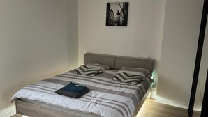 A neatly made bed with striped bedding and pillows, a bedside table with a lamp, and a wall-mounted picture.
