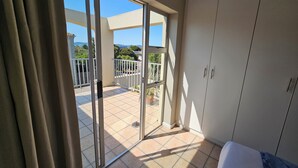 Une pièce dotée d’une porte-fenêtre coulissante donnant sur un balcon avec vue sur la verdure et un immeuble.